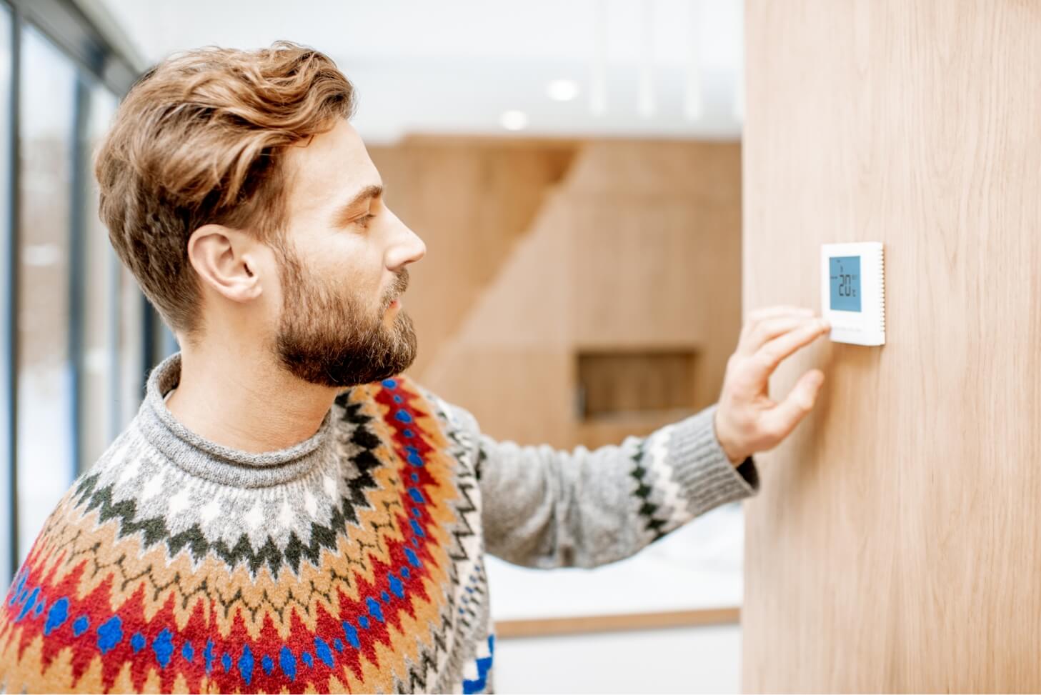 Man adjusting thermostat in a guide for setting up an energy monitor to track home energy usage.