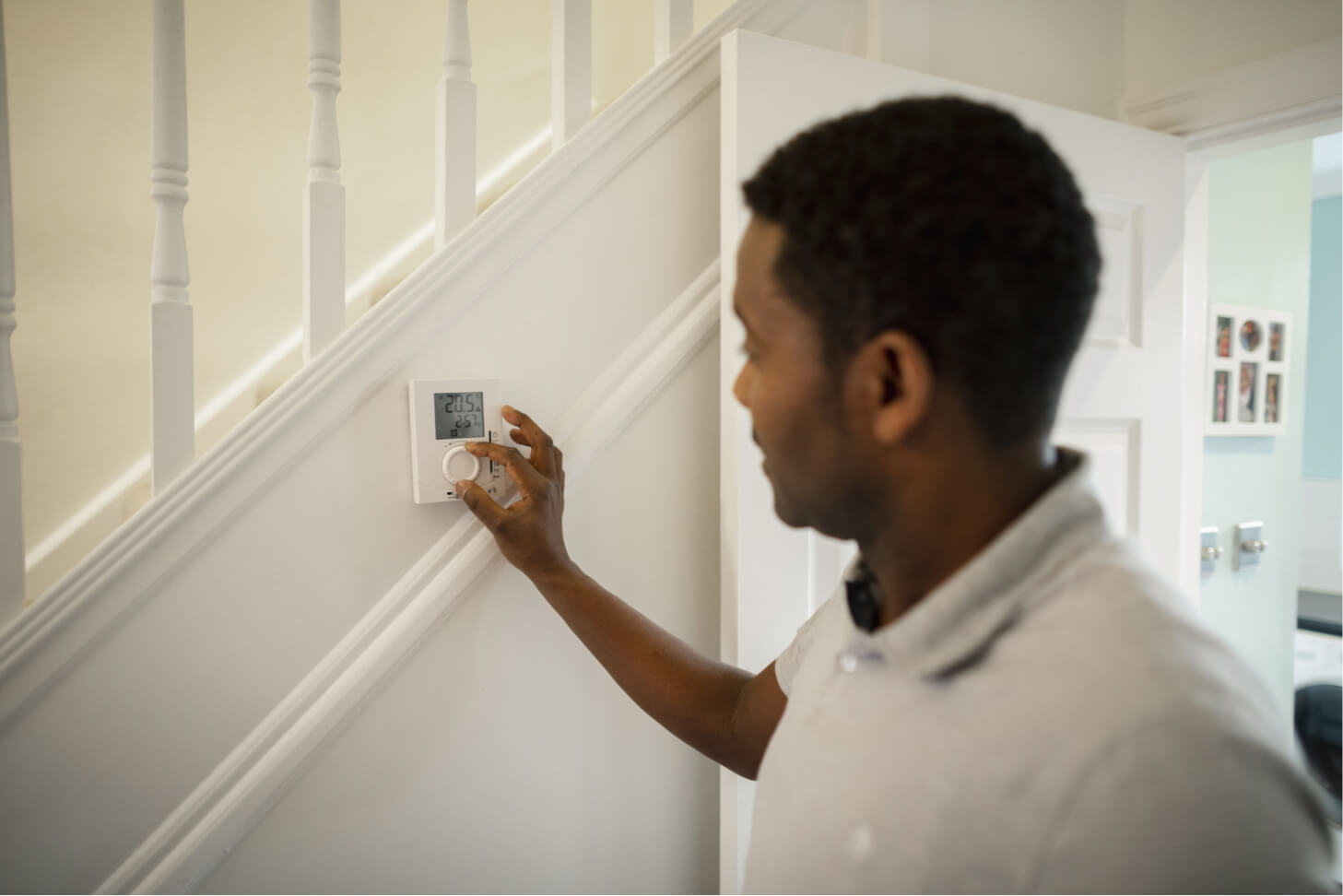 Man adjusting a thermostat while considering switching energy provider for better efficiency.